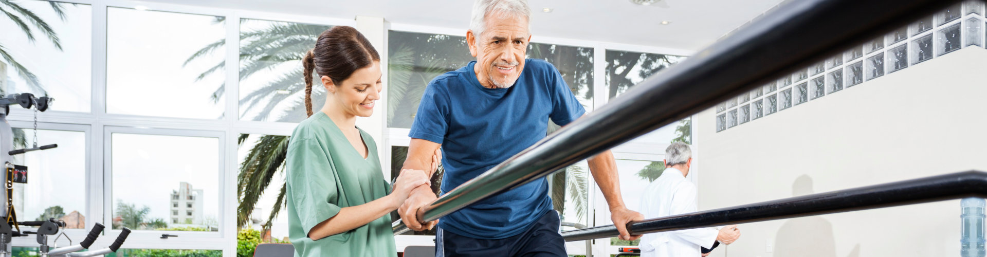 Physiotherapist Standing By Smiling Patient Walking Between Para